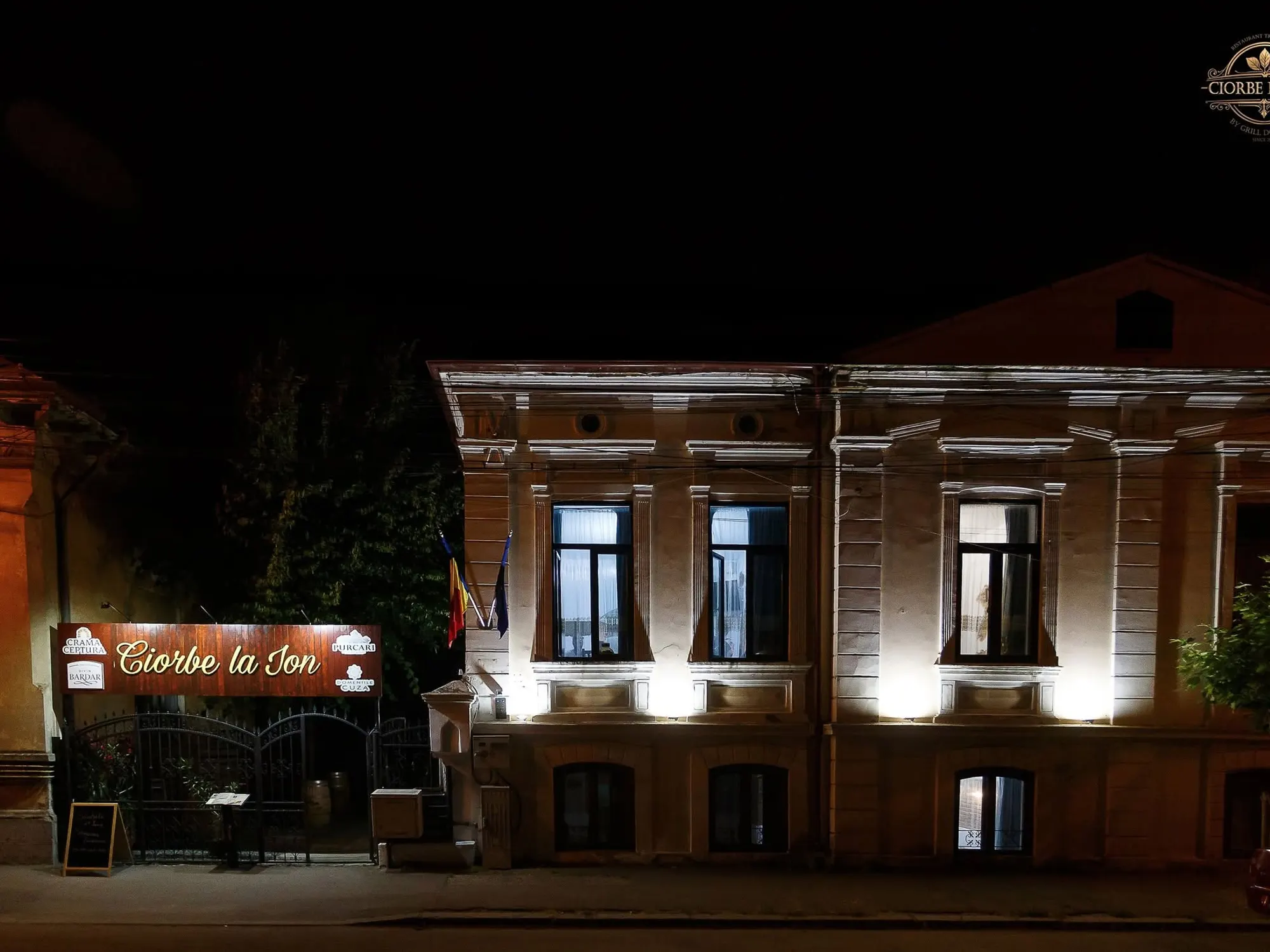 Clădirea restaurantului seara, cu fațada luminată și firma la poartă
