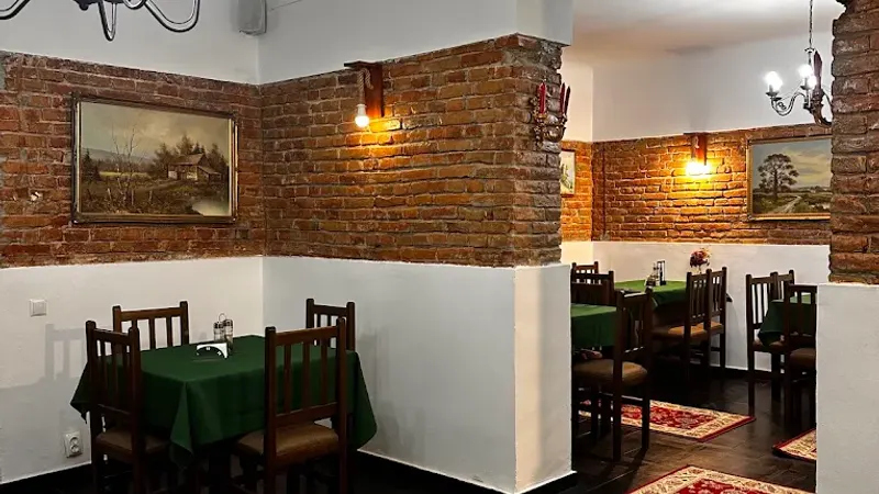 Colț de salon cu pereți de cărămidă, tablouri și mese cu fețe verzi
