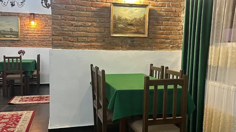 Masă cu față verde lângă un perete de cărămidă, sub tablouri înrămate