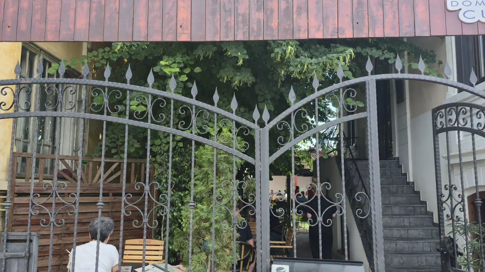 Poartă de fier forjat spre curtea cu terasă, umbrită de verdeață